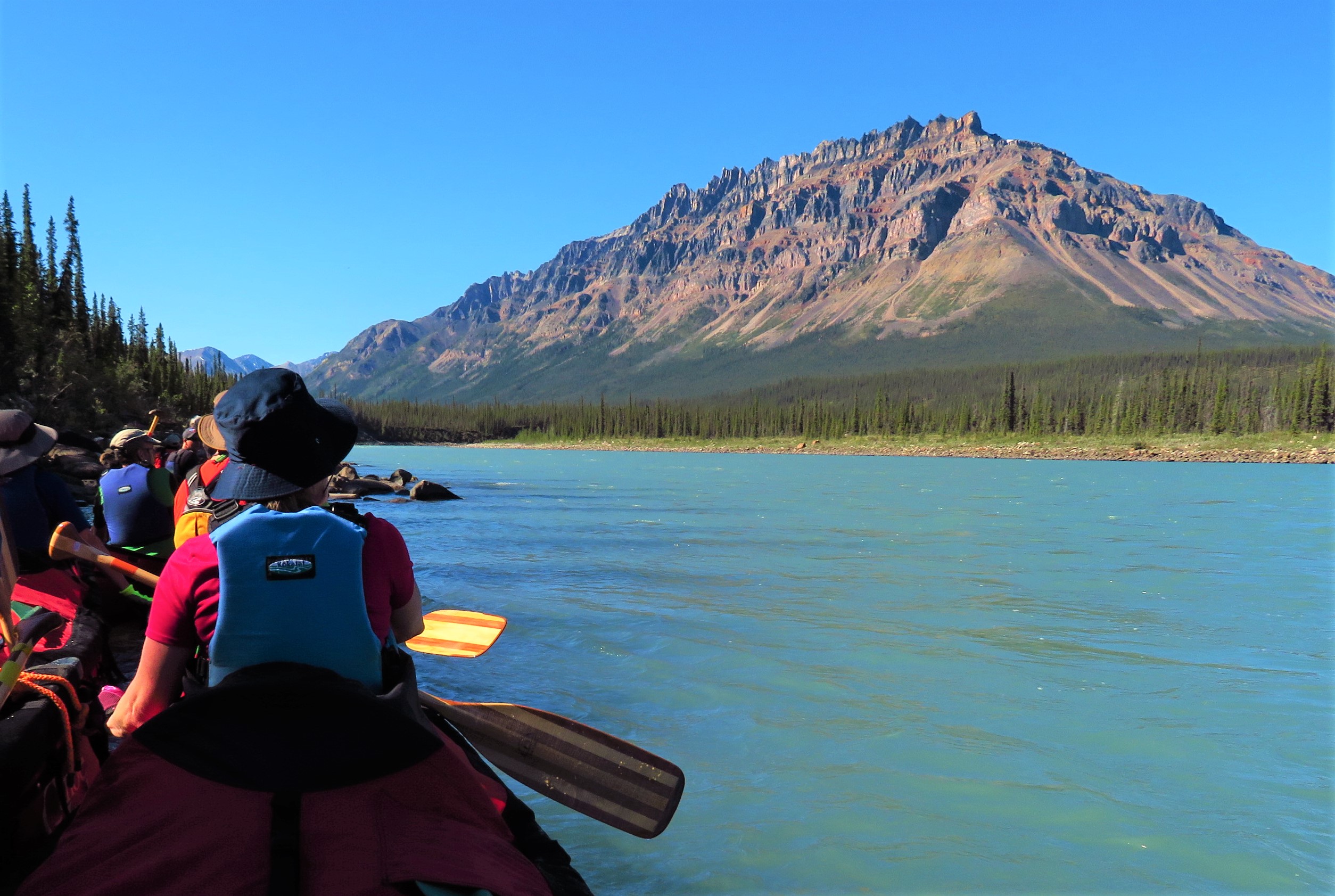 A lady sits in a canoe and looks up at Delthore mountain on the Keele River in Canada's Northwest Territories
